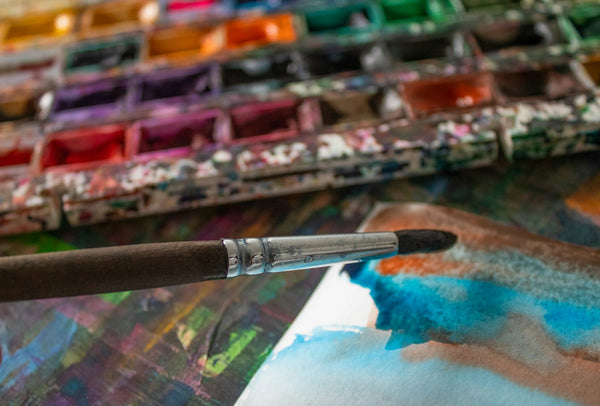 Pinceau devant une palette d'aquarelle aux teintes roses et jaunes